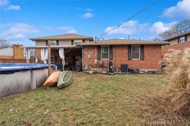 rear view of property with central AC unit, a yard, and a covered pool