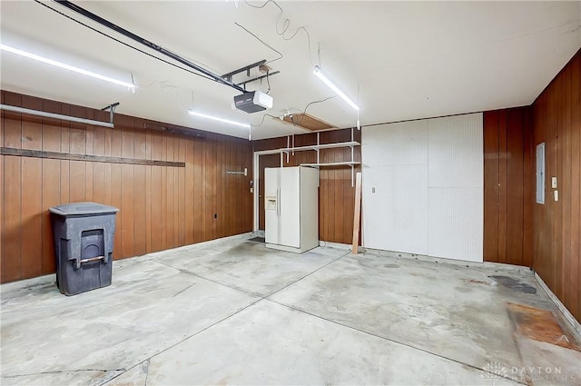 garage featuring a garage door opener, white refrigerator with ice dispenser, and wood walls