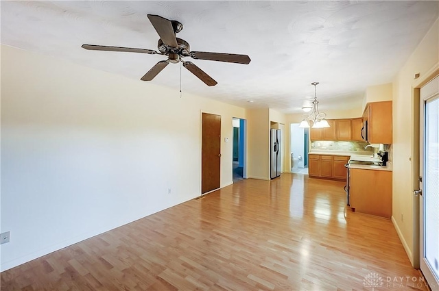 kitchen featuring stainless steel fridge, range, decorative backsplash, decorative light fixtures, and light wood-type flooring