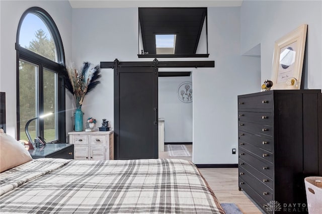 bedroom with a towering ceiling, a barn door, and light wood-type flooring