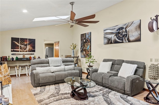 living room featuring ceiling fan, lofted ceiling with skylight, and light wood-type flooring