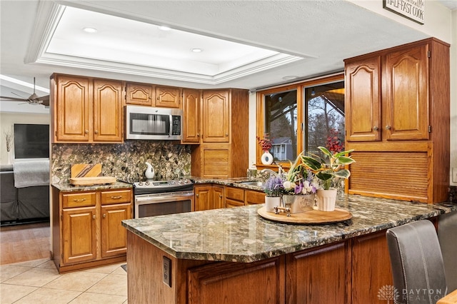 kitchen featuring light tile patterned flooring, dark stone countertops, decorative backsplash, a tray ceiling, and stainless steel appliances