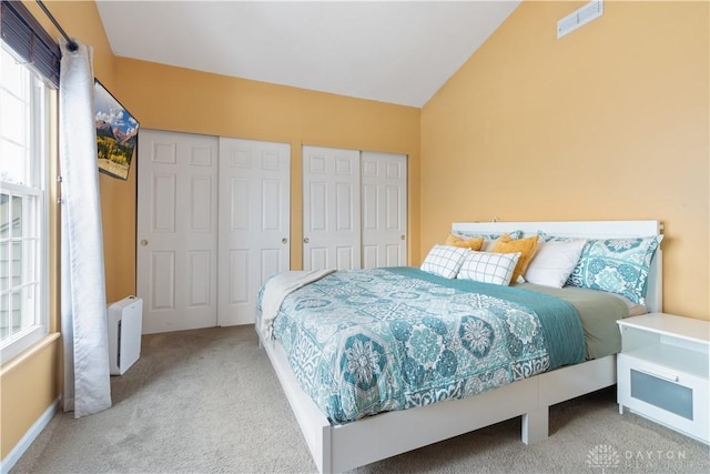 bedroom with radiator heating unit, vaulted ceiling, carpet floors, and two closets