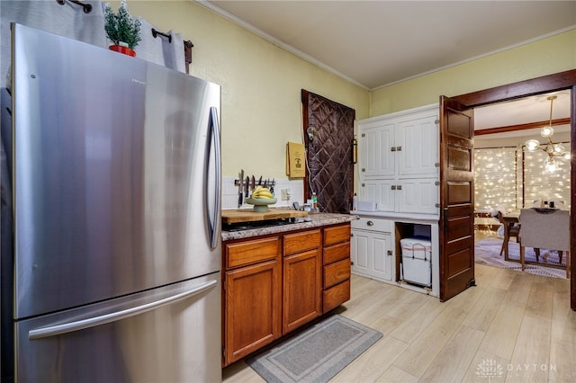 kitchen with crown molding, stainless steel refrigerator, a notable chandelier, light hardwood / wood-style floors, and decorative light fixtures