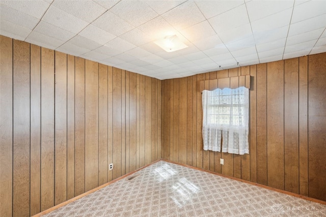 carpeted spare room with wood walls and visible vents