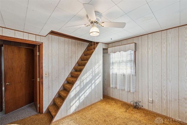 stairway with wood walls, carpet flooring, and a ceiling fan