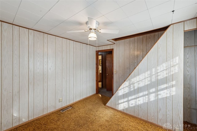 spare room with wood walls, carpet, visible vents, and a ceiling fan