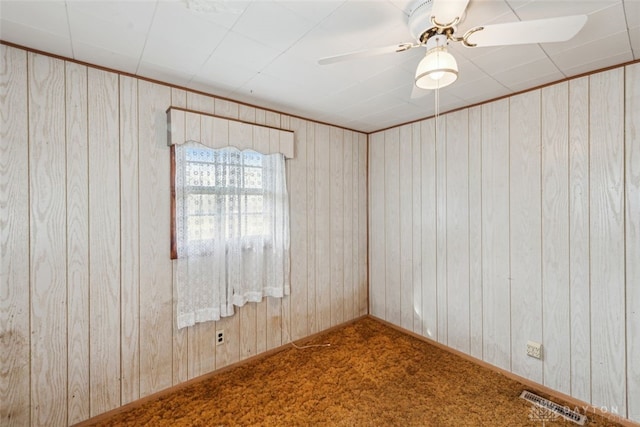 carpeted empty room with a ceiling fan, visible vents, and wood walls