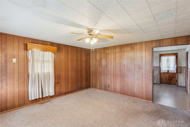 carpeted spare room with baseboards, a ceiling fan, visible vents, and wooden walls