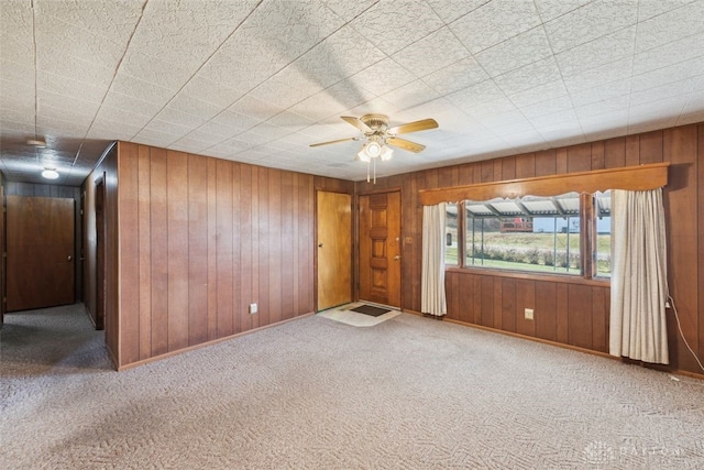 spare room with carpet, wood walls, baseboards, and ceiling fan