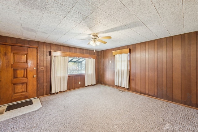 spare room with a ceiling fan, carpet flooring, wood walls, and baseboards