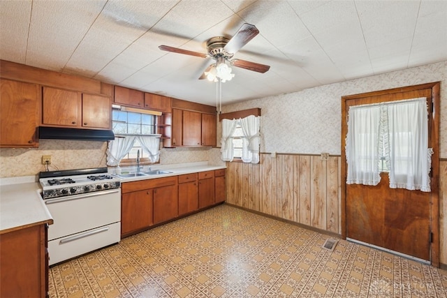 kitchen featuring light countertops, wainscoting, a sink, under cabinet range hood, and white gas range oven