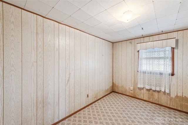 carpeted empty room featuring wood walls and baseboards