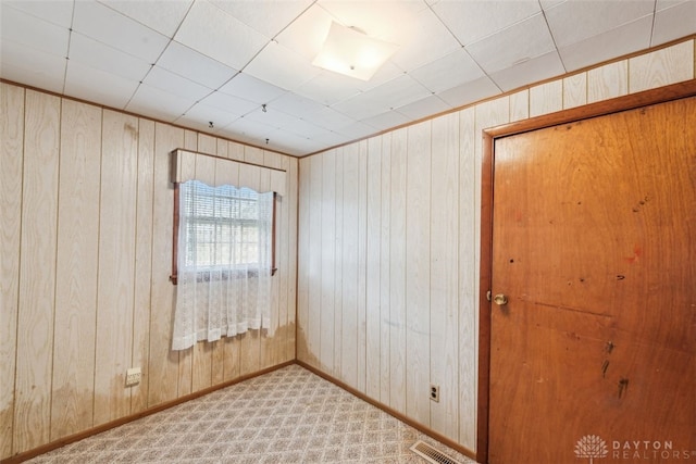 carpeted spare room with visible vents, wooden walls, and baseboards