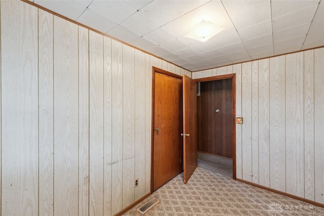 carpeted spare room with baseboards, wooden walls, and visible vents