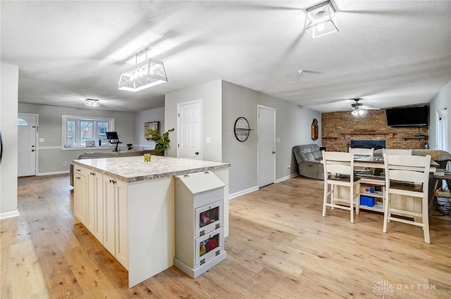 kitchen with ceiling fan, a fireplace, a kitchen island, and light hardwood / wood-style flooring