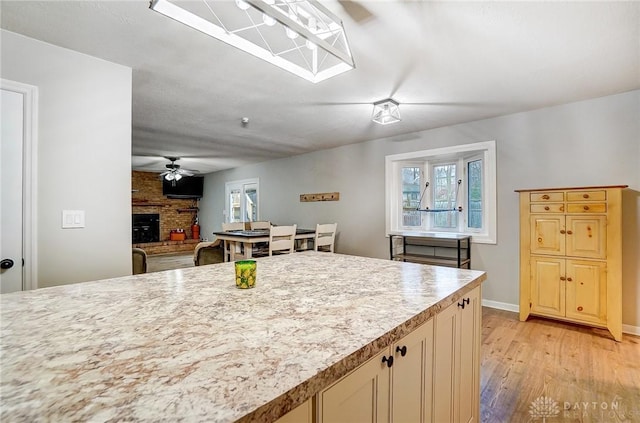 kitchen with ceiling fan, a brick fireplace, and light hardwood / wood-style flooring