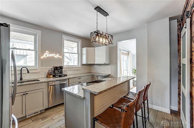 kitchen with sink, appliances with stainless steel finishes, hanging light fixtures, light stone counters, and a kitchen bar