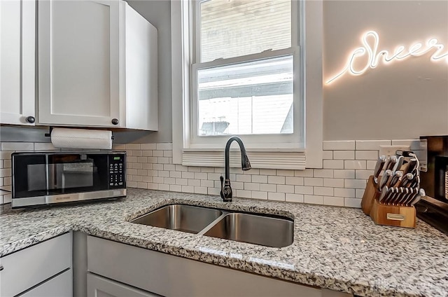 kitchen featuring sink, decorative backsplash, light stone countertops, and white cabinets