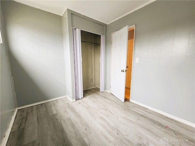 unfurnished bedroom featuring crown molding, light hardwood / wood-style flooring, and a closet