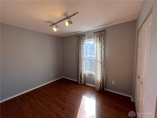 spare room featuring dark wood-type flooring, a textured ceiling, and track lighting