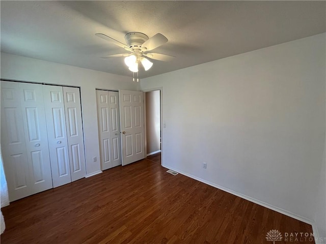 unfurnished bedroom with two closets, dark wood-type flooring, and ceiling fan