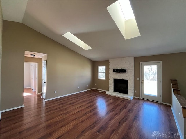 unfurnished living room featuring plenty of natural light, dark hardwood / wood-style floors, a stone fireplace, and a skylight