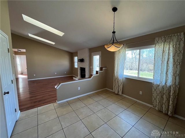 unfurnished dining area with lofted ceiling with skylight, light tile patterned floors, and a fireplace