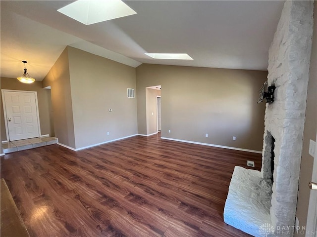 unfurnished living room with dark hardwood / wood-style flooring, a stone fireplace, and vaulted ceiling with skylight