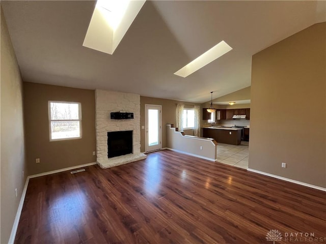 unfurnished living room with light hardwood / wood-style flooring, a fireplace, and lofted ceiling with skylight