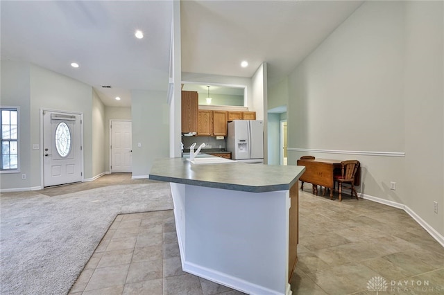 kitchen featuring high vaulted ceiling, sink, white fridge with ice dispenser, light colored carpet, and kitchen peninsula