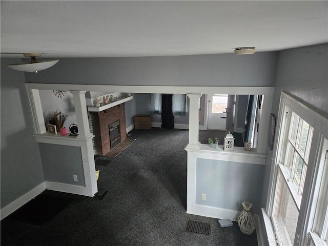 living room featuring a brick fireplace, visible vents, baseboards, and ornate columns