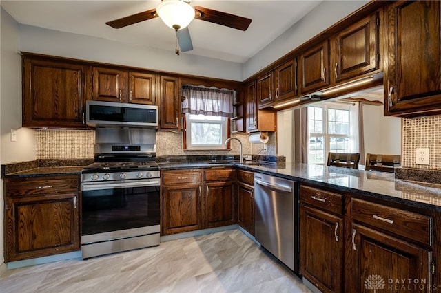 kitchen with backsplash, appliances with stainless steel finishes, sink, and dark stone countertops