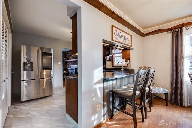 kitchen featuring sink, a breakfast bar area, crown molding, stainless steel fridge with ice dispenser, and a fireplace