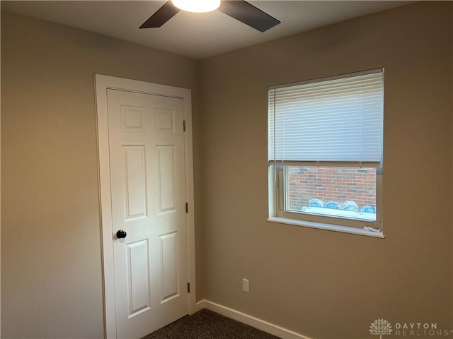 unfurnished bedroom with ceiling fan and dark carpet