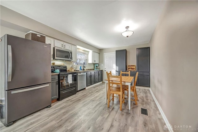 kitchen with white cabinetry, tasteful backsplash, gray cabinets, stainless steel appliances, and light hardwood / wood-style floors