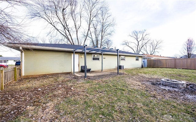 rear view of property with cooling unit, a fire pit, and a lawn