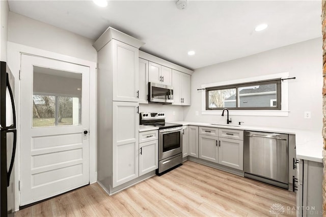 kitchen featuring stainless steel appliances, recessed lighting, light countertops, a sink, and light wood-type flooring