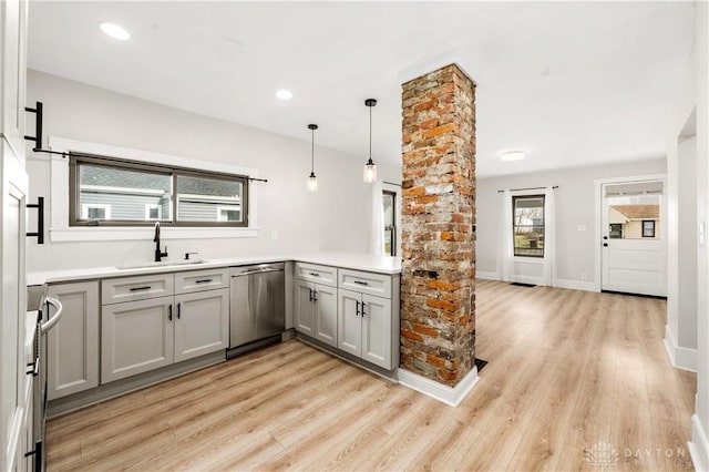 kitchen featuring light wood finished floors, appliances with stainless steel finishes, light countertops, pendant lighting, and a sink