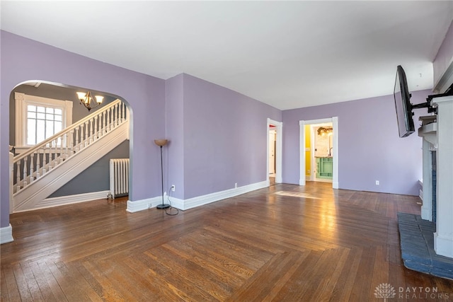 unfurnished living room with radiator, a fireplace, dark parquet floors, and a chandelier