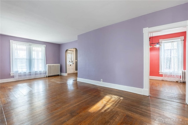 empty room featuring a wealth of natural light, baseboards, arched walkways, and radiator heating unit