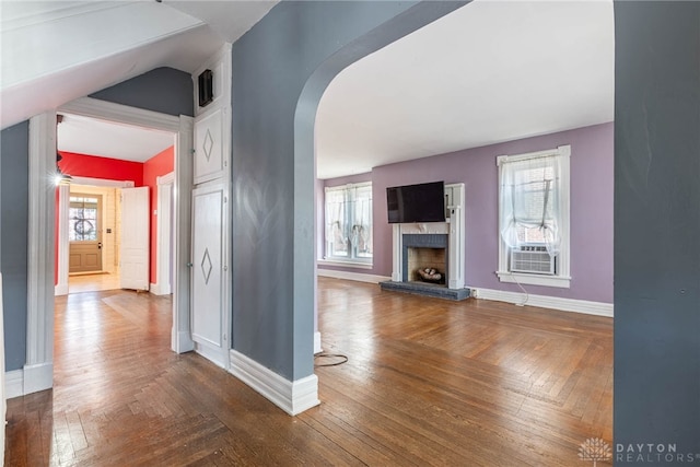 unfurnished living room with cooling unit, baseboards, arched walkways, and a fireplace with raised hearth