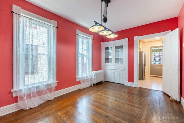 unfurnished dining area with radiator, baseboards, and wood finished floors