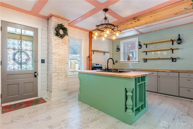 kitchen featuring wooden counters, a center island with sink, gray cabinets, light wood-style floors, and a sink