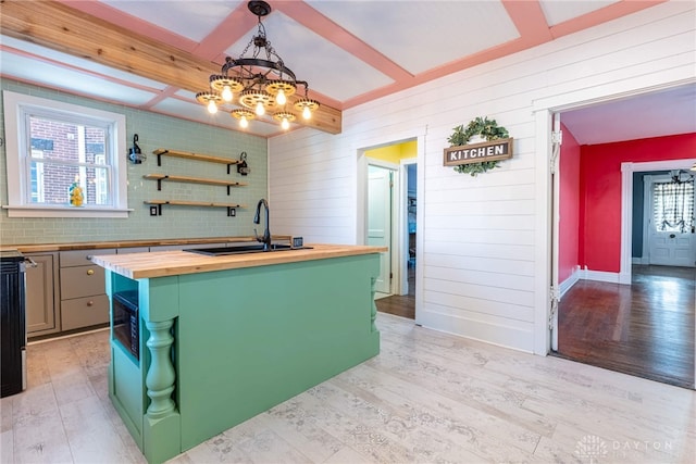 kitchen featuring sink, wooden counters, hanging light fixtures, light hardwood / wood-style floors, and a center island with sink