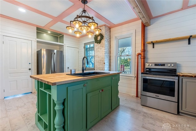 kitchen with sink, green cabinets, butcher block counters, appliances with stainless steel finishes, and a center island with sink