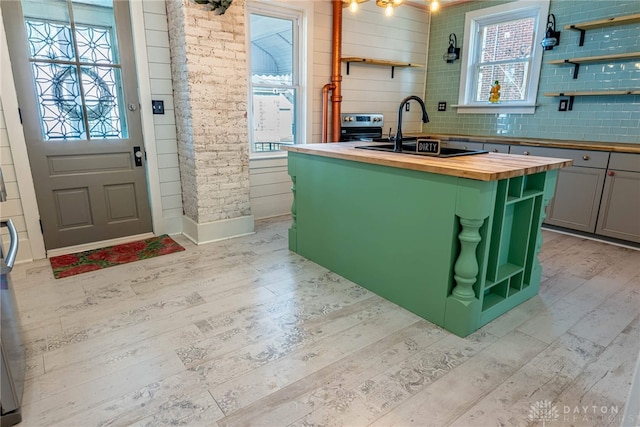 kitchen with a kitchen island with sink, butcher block countertops, light hardwood / wood-style floors, and sink