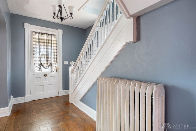 foyer entrance featuring an inviting chandelier, radiator heating unit, and dark parquet floors