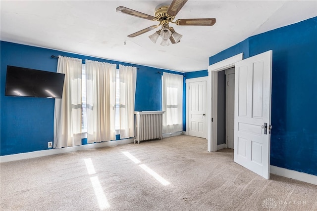 unfurnished bedroom featuring radiator, light colored carpet, and ceiling fan