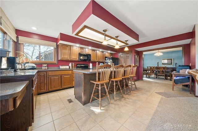 kitchen with decorative light fixtures, light tile patterned floors, a kitchen breakfast bar, a kitchen island, and black appliances